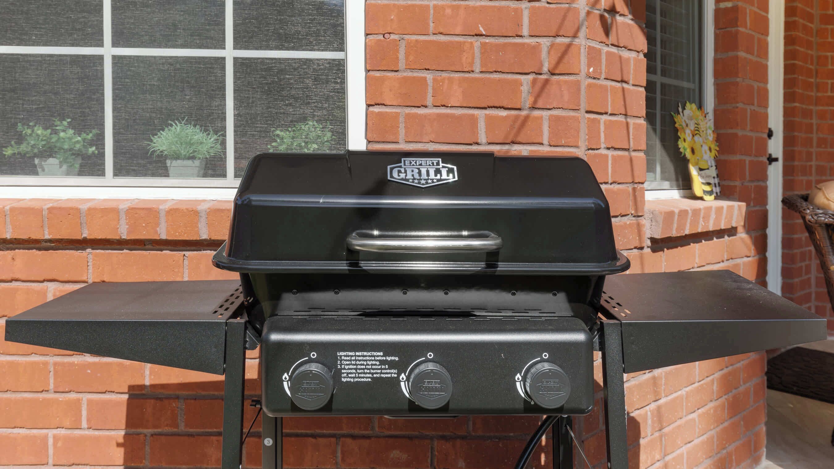A black grill with a 'Grill Expert' logo, two control knobs, and a window in the background.