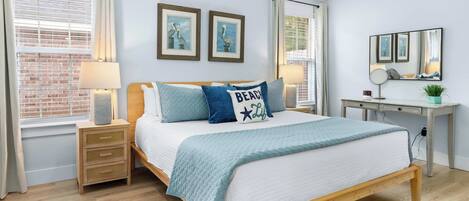 A bedroom with a wooden bed, two bedside tables with lamps, a desk with a mirror, and a window with blinds.