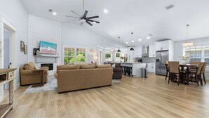 Ein geräumiges Wohnzimmer mit einer großen Couch, einem an der Wand montierten Fernseher und einem Essbereich mit Tisch und Stühlen.