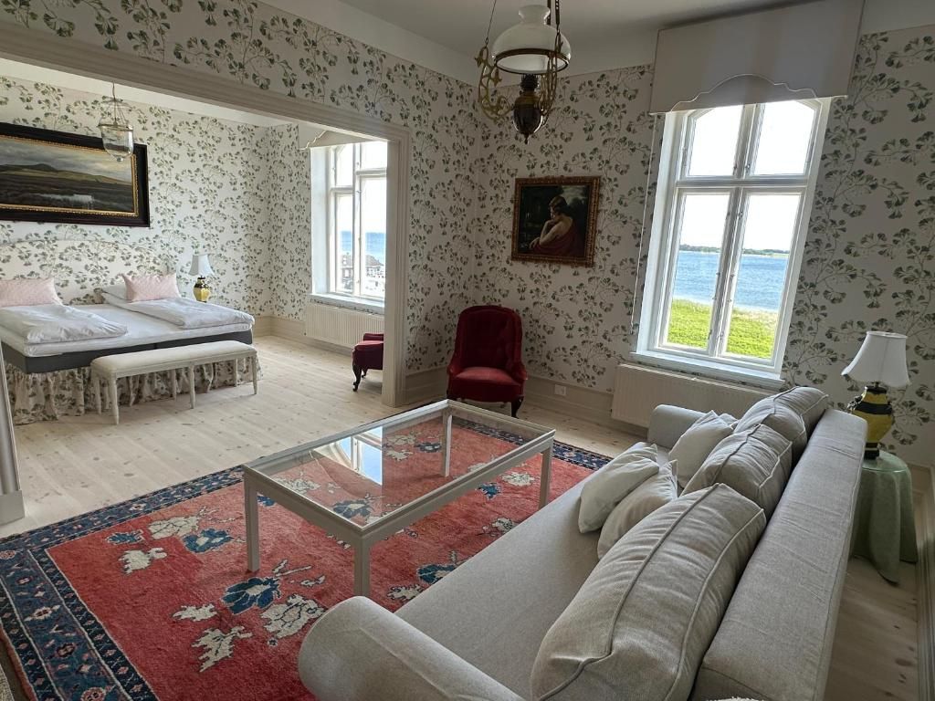 A spacious living room with a large sofa, a glass coffee table, and a view of the sea through large windows.