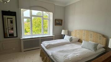 A bedroom with two beds, a window with a view, a radiator, and a lamp.
