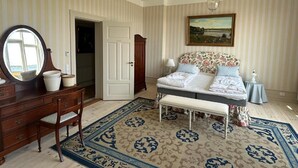 Un dormitorio con cama, cómoda, espejo, banca y un cuadro en la pared.