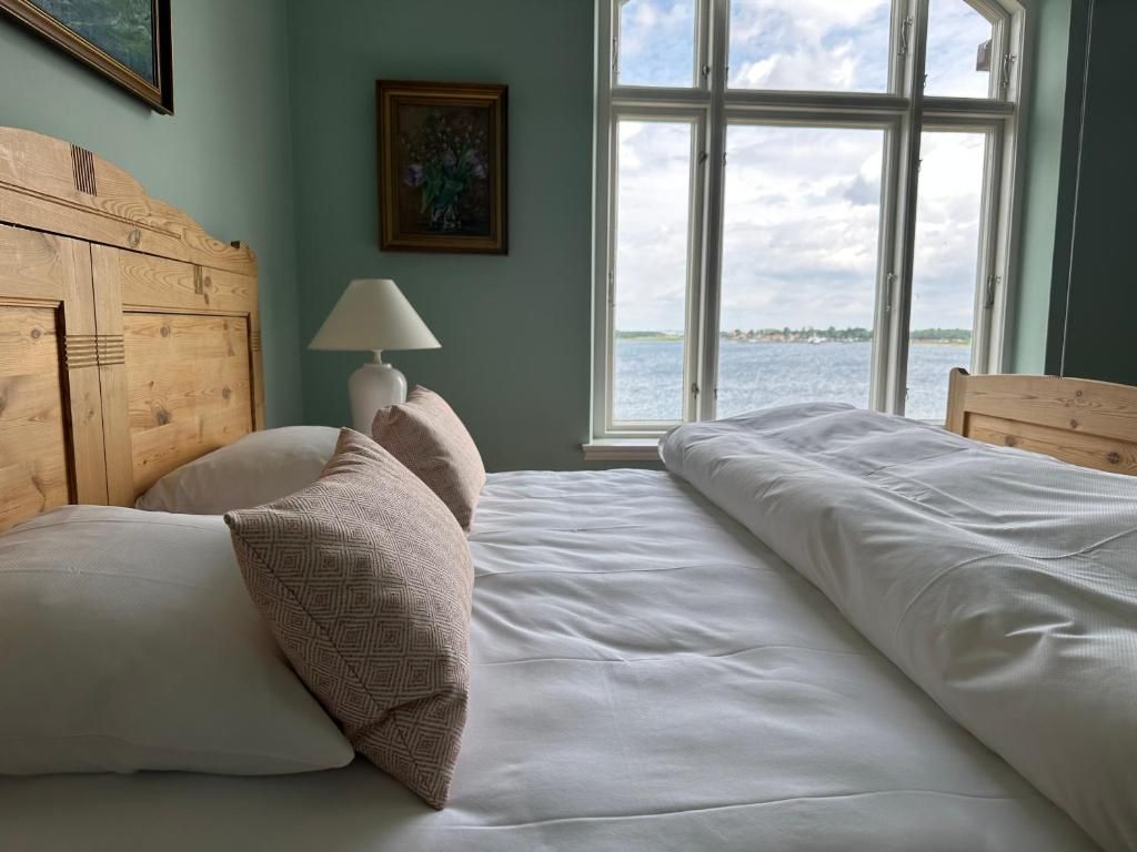 A bedroom with a wooden headboard, a bedside lamp, and a view of the water through a large window.