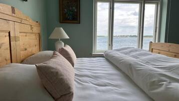 A bedroom with a wooden headboard, a bedside lamp, and a view of the water through a large window.