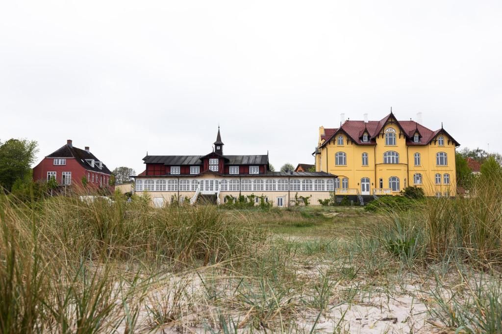 A row of three houses with distinct architectural styles, set against a backdrop of tall grass and a cloudy sky.
