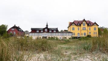 A row of three houses with distinct architectural styles, set against a backdrop of tall grass and a cloudy sky.