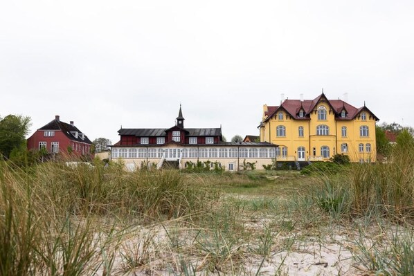 A row of three houses with distinct architectural styles, set against a backdrop of tall grass and a cloudy sky. - Aaroesund Badehotel (Haderslev)