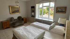 A bedroom with two beds, a window with a view, a hanging light fixture, and a chair. - Aaroesund Badehotel (Haderslev)