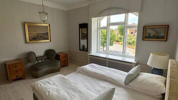 A bedroom with two beds, a window with a view, a hanging light fixture, and a chair.