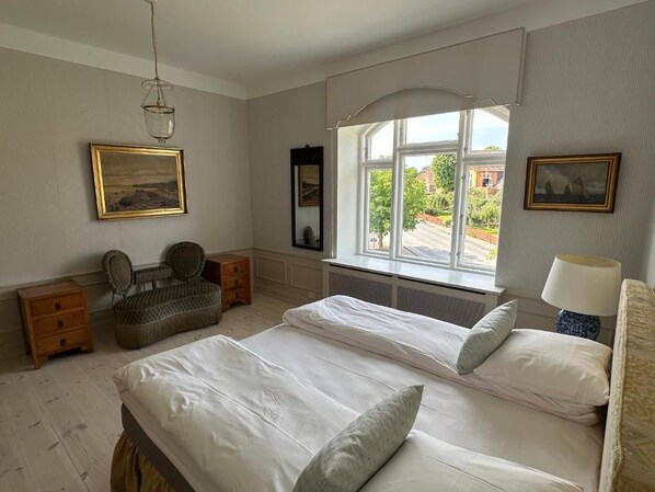 A bedroom with two beds, a window with a view, a hanging light fixture, and a chair. - Aaroesund Badehotel (Haderslev)
