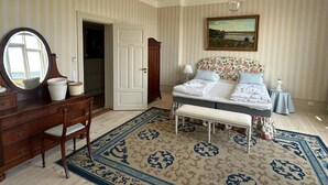 A bedroom with a bed, a dresser, a mirror, a bench, and a painting on the wall. - Aaroesund Badehotel (Haderslev)