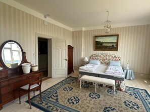 A bedroom with a bed, a dresser, a mirror, a bench, and a painting on the wall. - Aaroesund Badehotel (Haderslev)