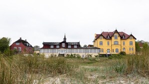 Tres casas en fila con estilos arquitectónicos diferentes, con un fondo de hierba alta y un cielo nublado.