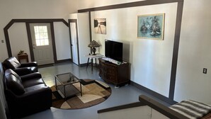 A living room with a sofa, a coffee table, a TV, and a painting on the wall. - Furnished Studio with washer and dryer, and pool! (Ukiah)