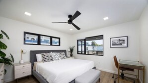 A bedroom with a bed, a desk, a chair, a ceiling fan, and framed pictures on the wall. - Charming Ocean View 2-bedroom apartment with AC in Del Mar! (Del Mar)