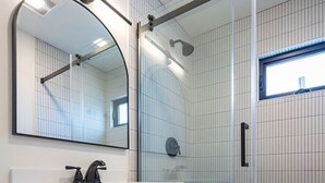 A modern bathroom with a wooden vanity, a large mirror, and a glass-enclosed shower area. - Charming Ocean View 2-bedroom apartment with AC in Del Mar! (Del Mar)