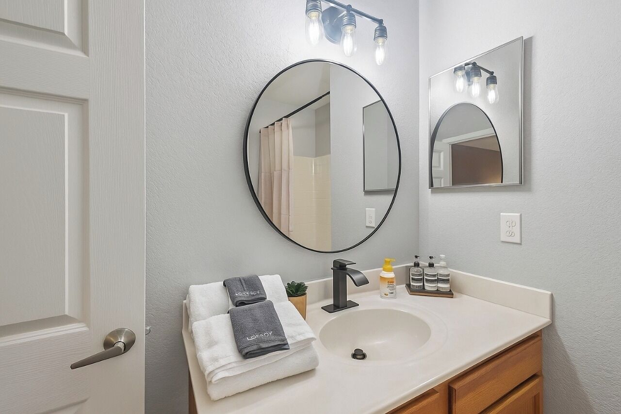 Une salle de bain avec un lavabo blanc, un miroir rond et un porte-serviettes avec des serviettes.