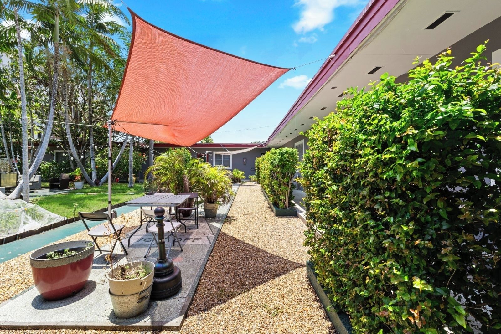 Un patio con mesa y sillas, rodeado de plantas en macetas y una piscina.