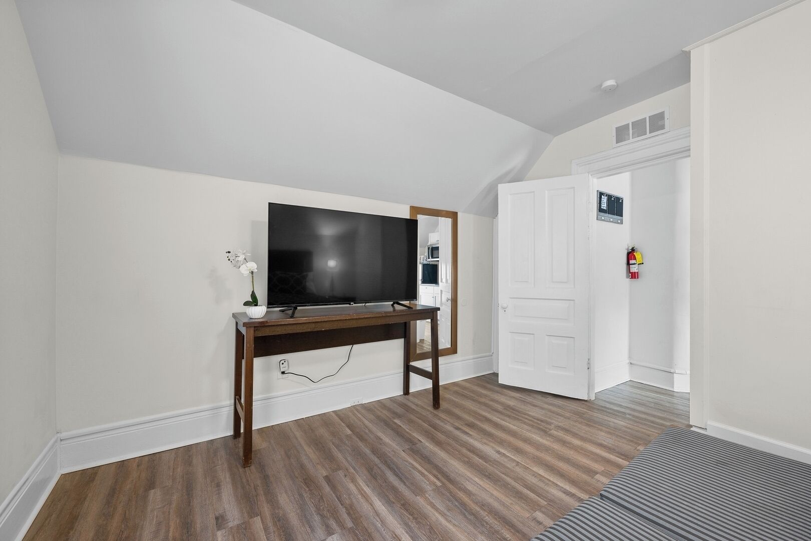 A room with a wooden TV stand, a flat-screen TV, a white door, and a fire extinguisher.