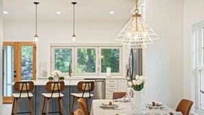 Een moderne eethoek met een witte tafel voor vier personen, omringd door houten stoelen en een grote hanglamp.