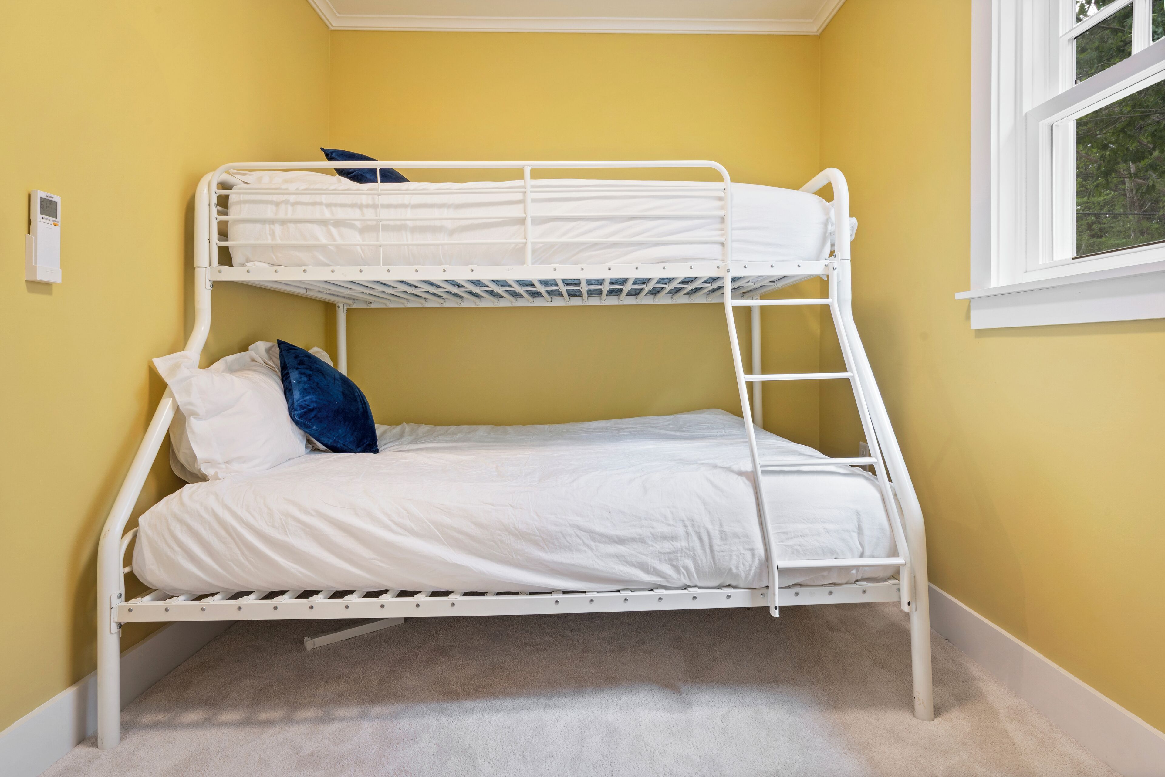 Una cama individual en un dormitorio con paredes amarillas y una ventana.