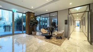A modern hotel lobby with a glass wall, a large potted plant, comfortable seating, and a clean, polished floor.