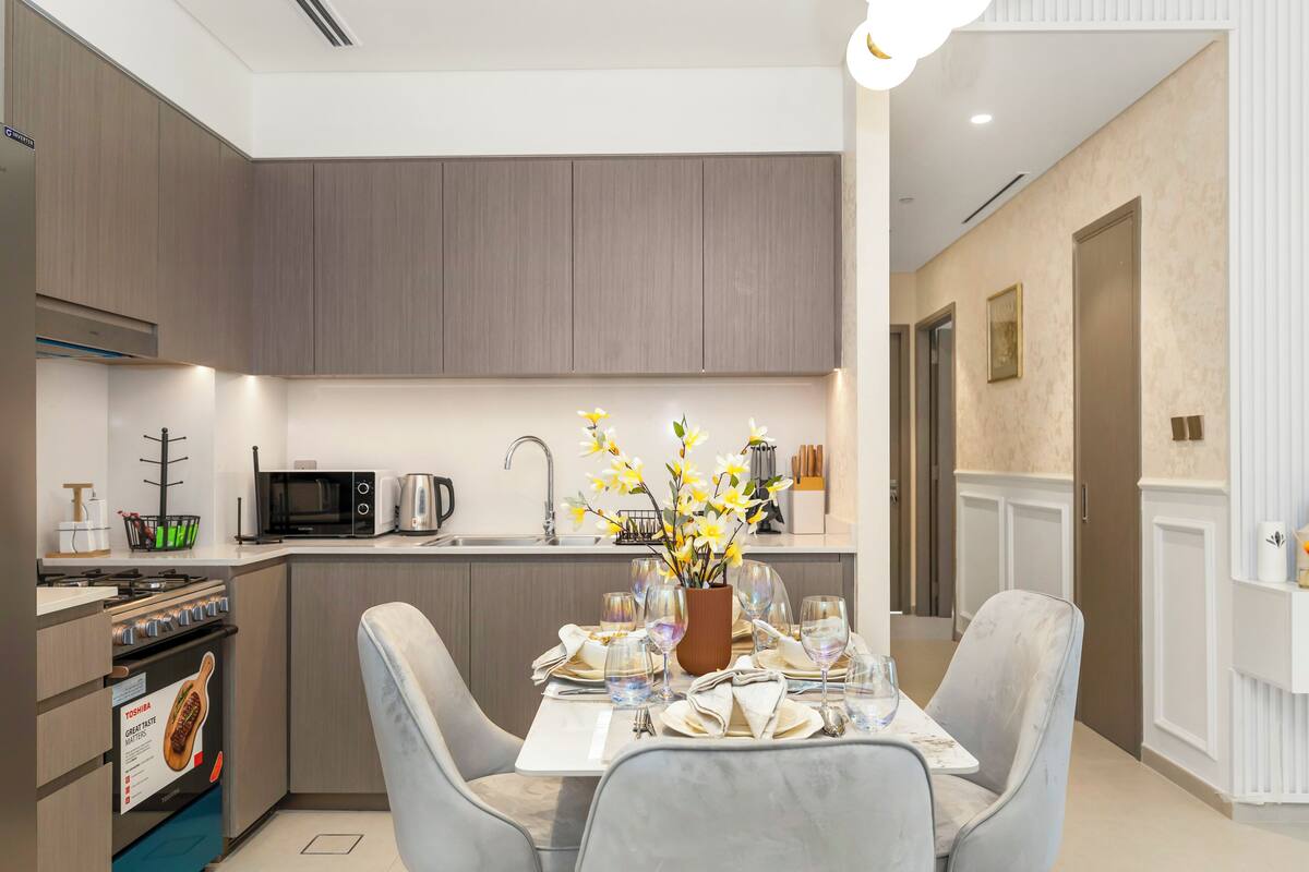 A modern kitchen with grey cabinets, a built-in microwave, and a dining area with a table set for two.