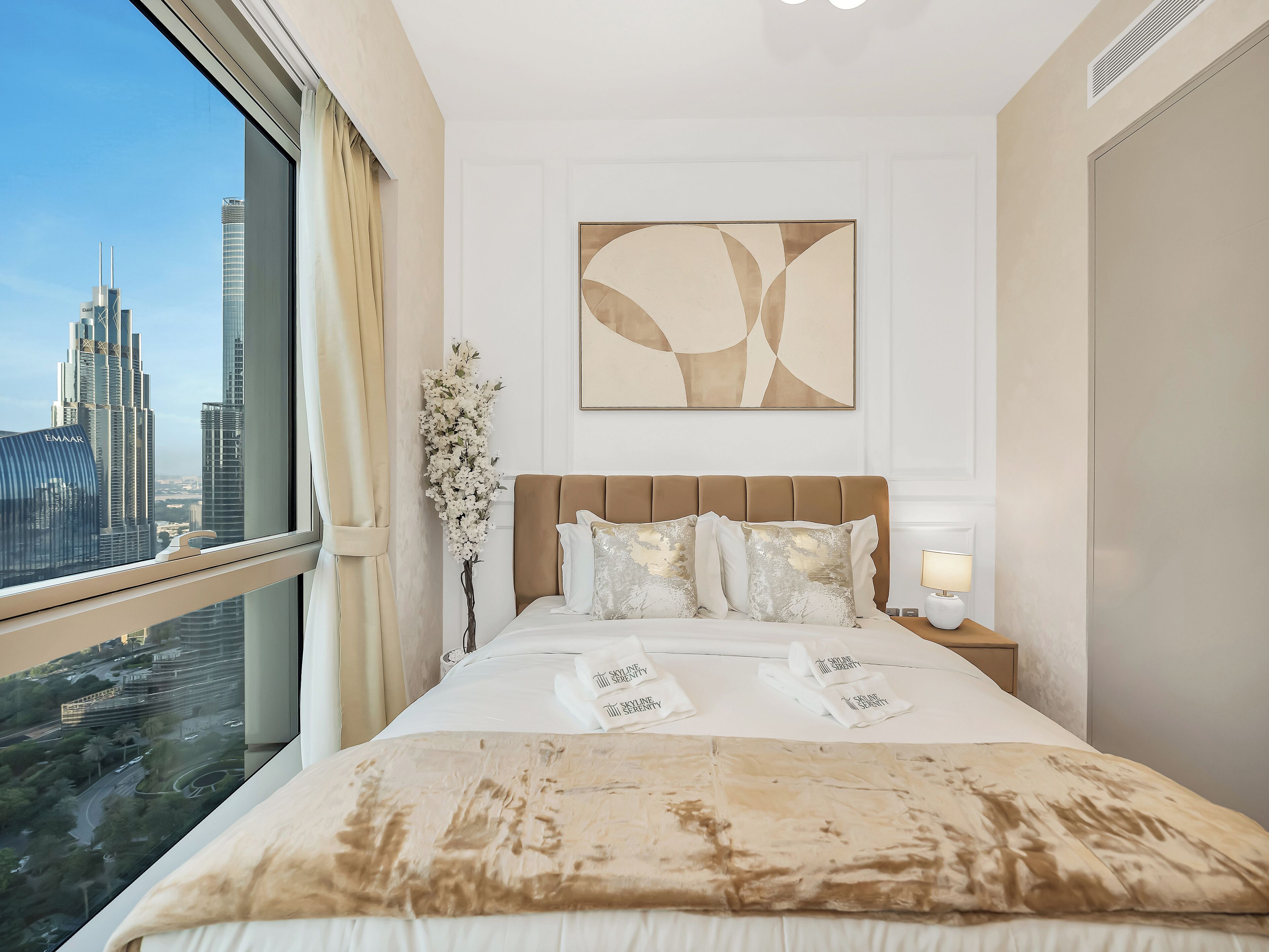 Habitación de hotel con una cama grande, vistas a un paisaje urbano y un cuadro abstracto moderno en la pared.