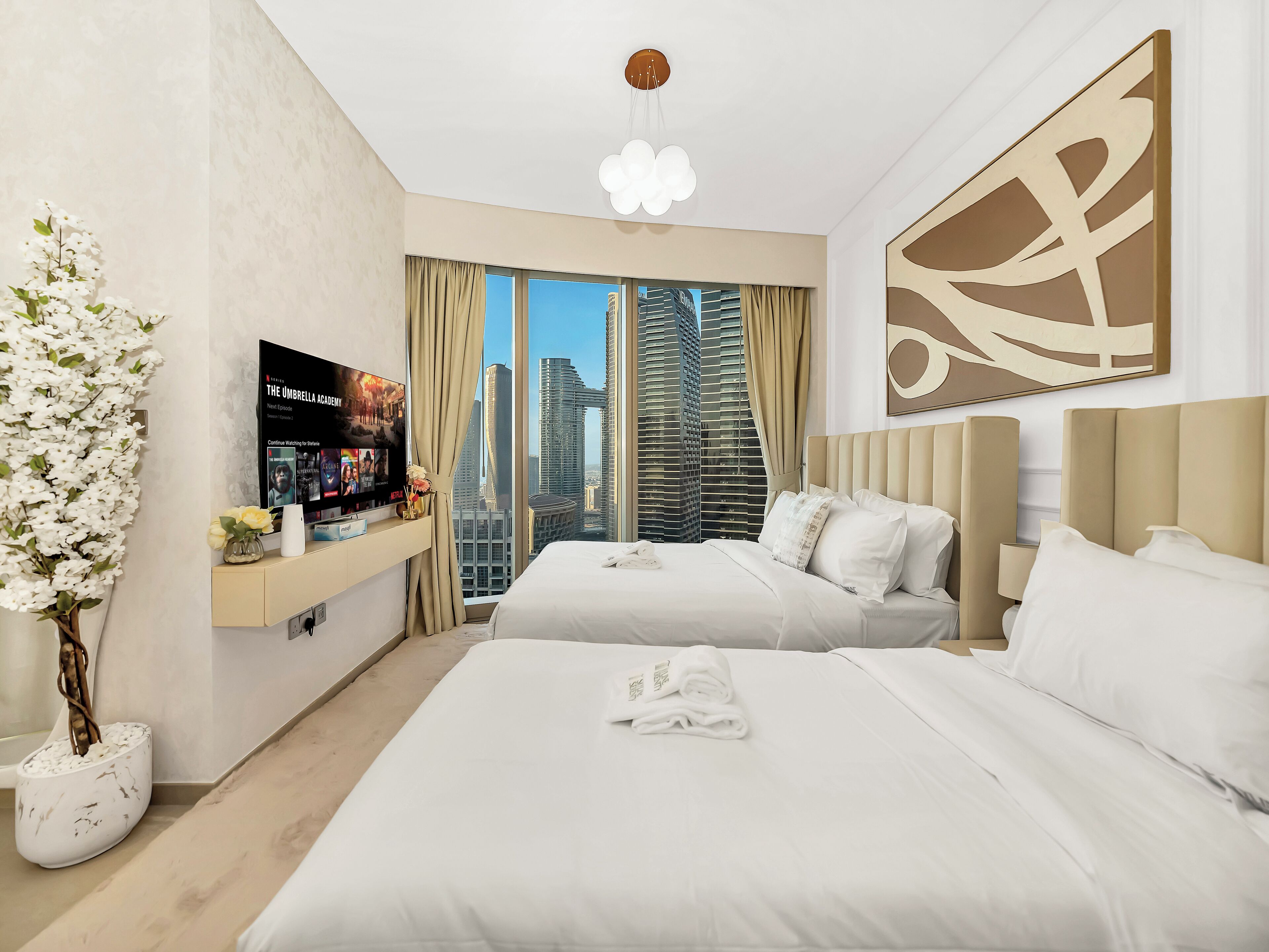 A modern hotel room with a large bed, a TV on the wall, and a view of tall buildings.