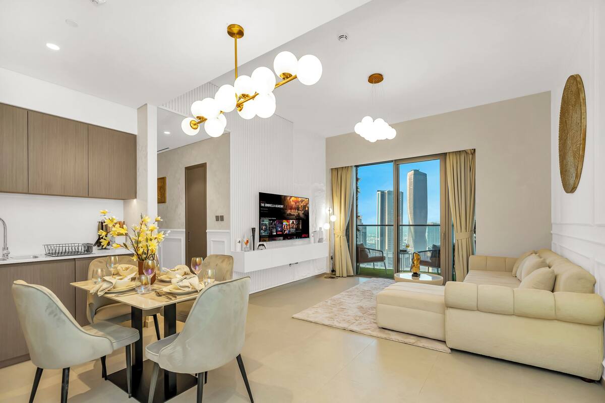 A modern living room with a sofa, dining area with chairs, a TV, and a city view through large windows.