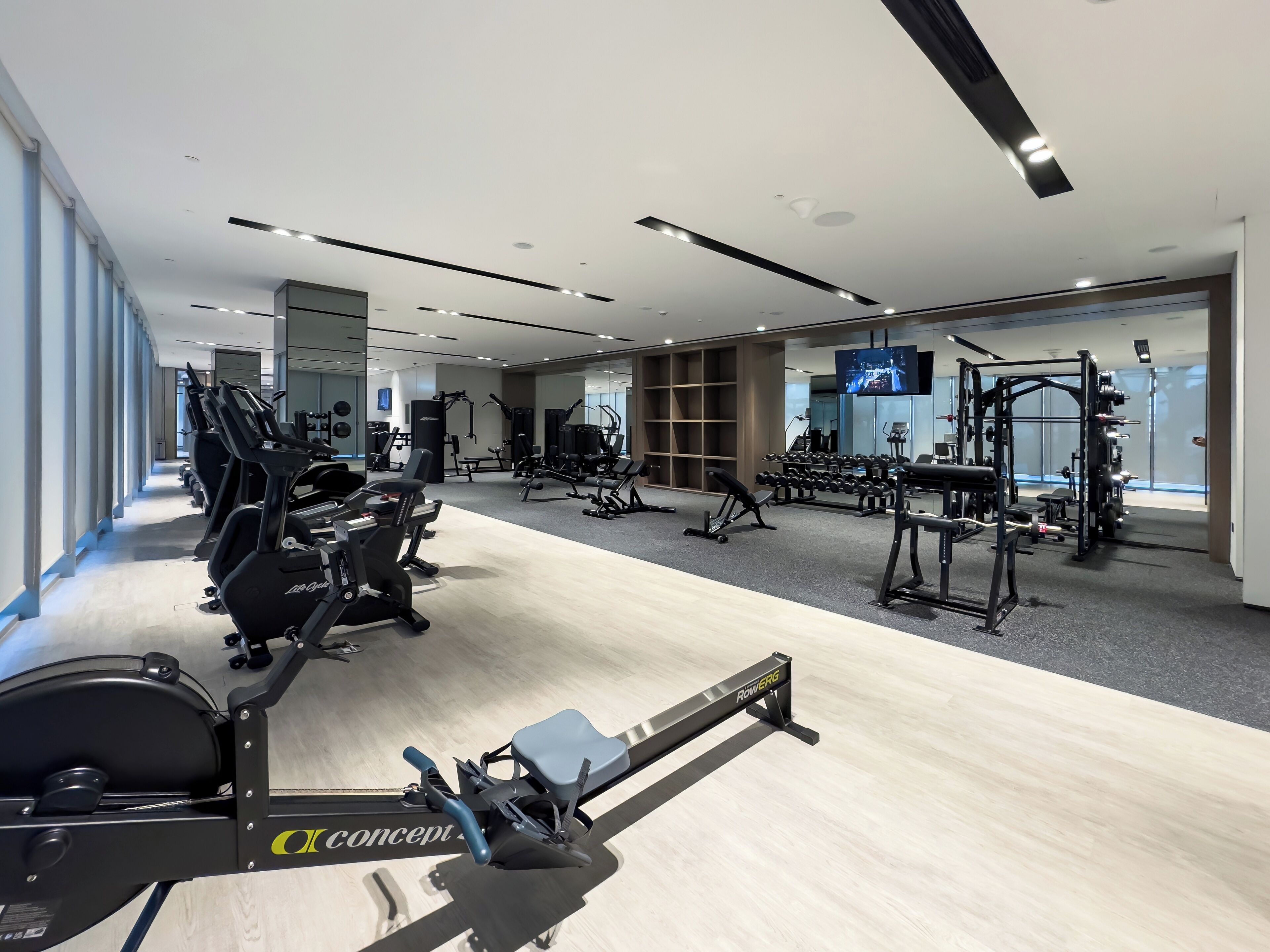 A modern gym with cardio machines, weightlifting equipment, and a TV screen.