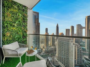 A balcony with a city view, a wicker chair, a small table with a box of chocolates and two glasses of wine, and a green wall with plants. - Skyline Grandeur I Burj & Fountain View (Dubai)