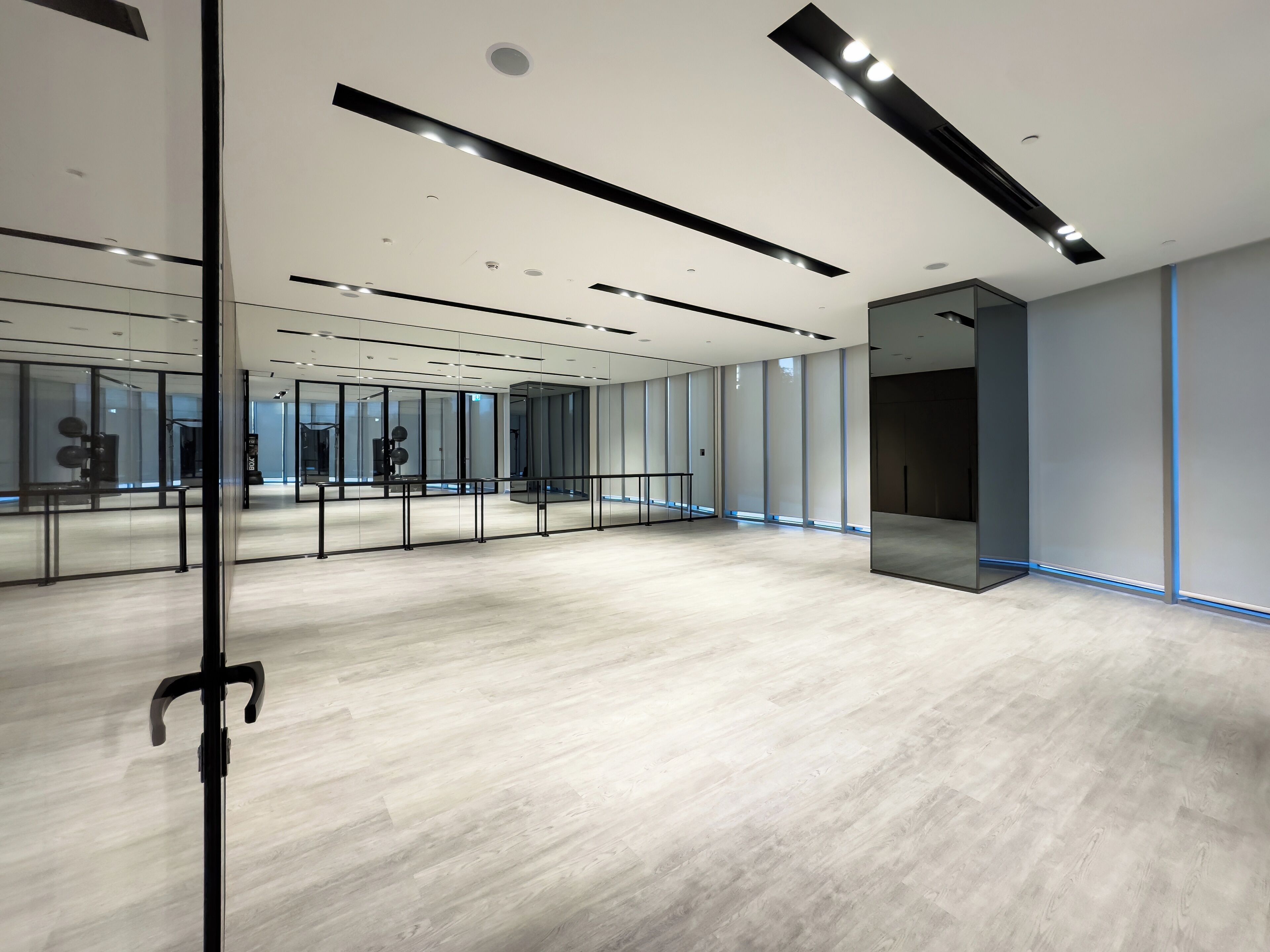 Une pièce spacieuse et moderne, dotée d’un plancher en bois, de murs en verre et d’un grand miroir.