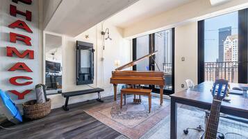 Een ruime kamer met een vleugelpiano, een gitaar en een groot raam met uitzicht over de stad.