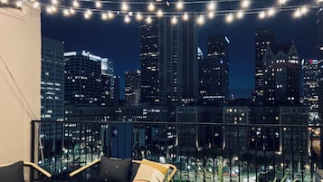 Een balkon met lichtslingers, twee zwarte stoelen en een uitzicht op een stadshemel bij nacht.