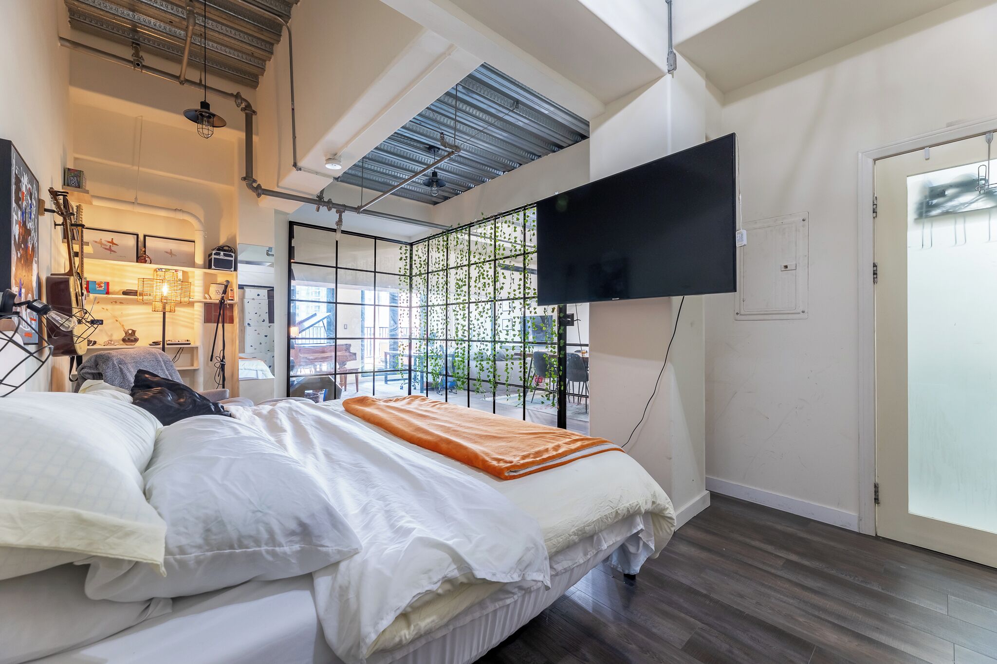 Een moderne slaapkamer met een bed, een aan de muur bevestigde televisie en uitzicht op de omgeving via een raam.
