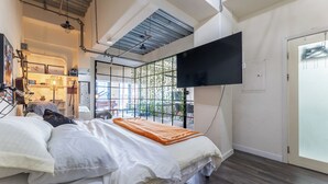 A modern bedroom with a bed, a TV mounted on the wall, and a view of the outdoors through a window. - Sun-Soaked Urban-Chic Retreat in DTLA (Los Angeles)