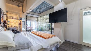 Een moderne slaapkamer met een bed, een aan de muur bevestigde televisie en uitzicht op de omgeving via een raam.