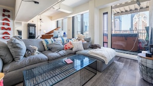A modern living room with a grey sofa, a glass coffee table, and a large window with a city view. - Sun-Soaked Urban-Chic Retreat in DTLA (Los Angeles)