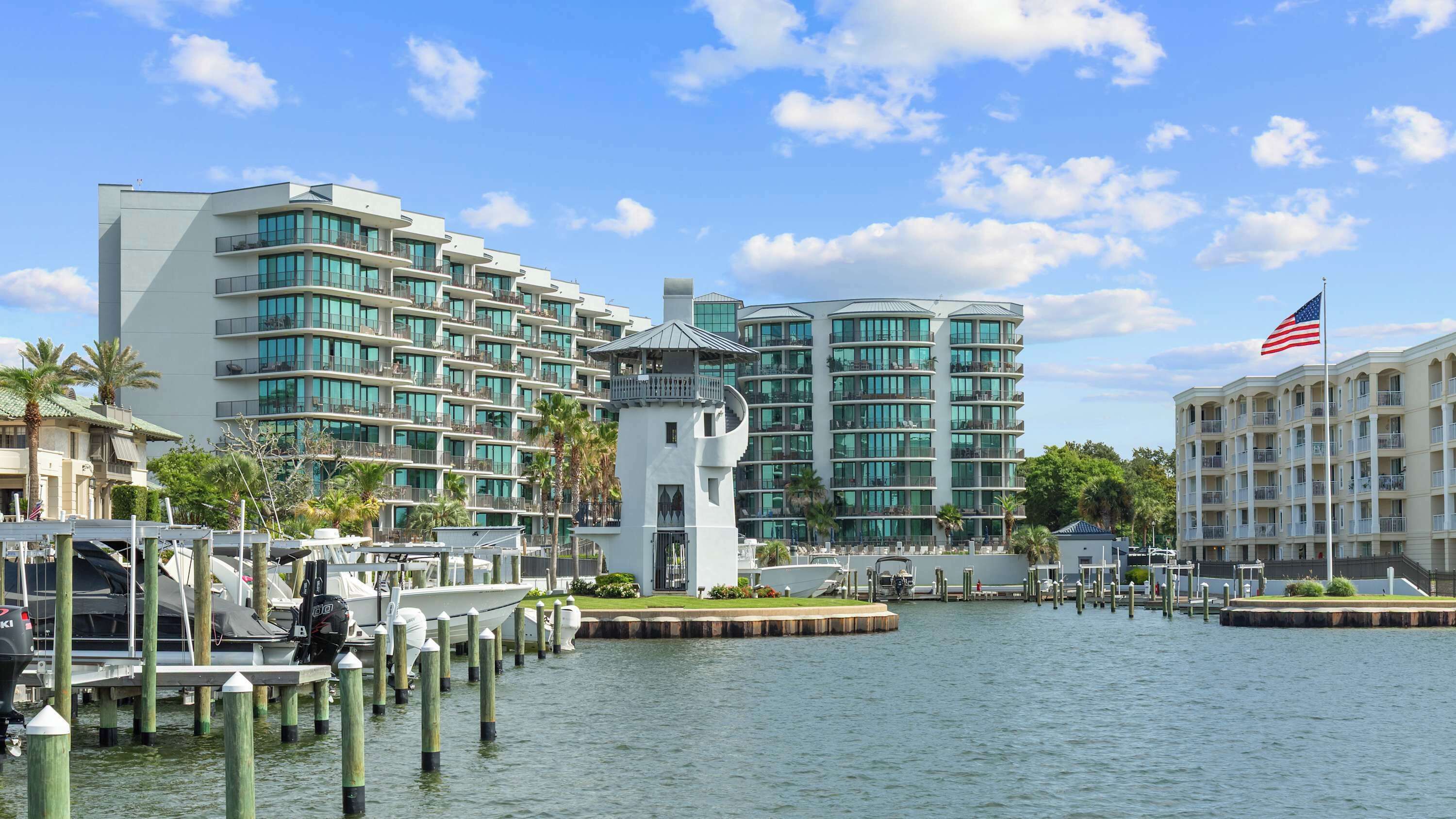 A waterfront hotel with multiple high-rise buildings, a dock with boats, and an American flag.