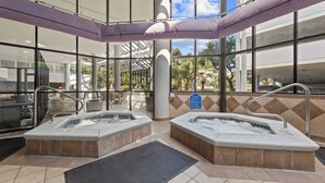 Ein Wellnessbereich mit zwei Whirlpools, einem durch eine Glasscheibe abgetrennten Bereich und Blick auf Palmen.