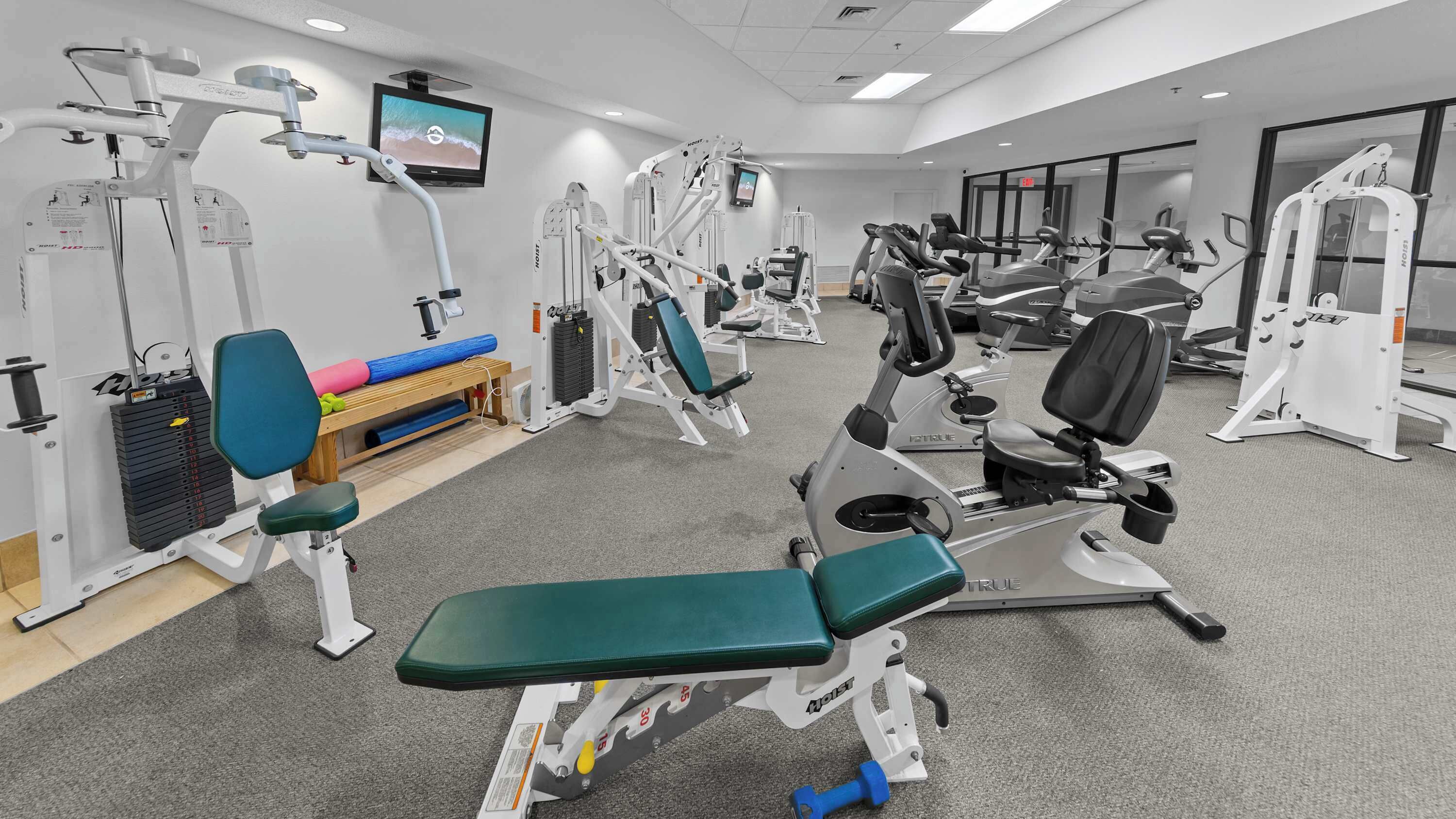 A gym with various exercise equipment, including treadmills, weight machines, and a bench.