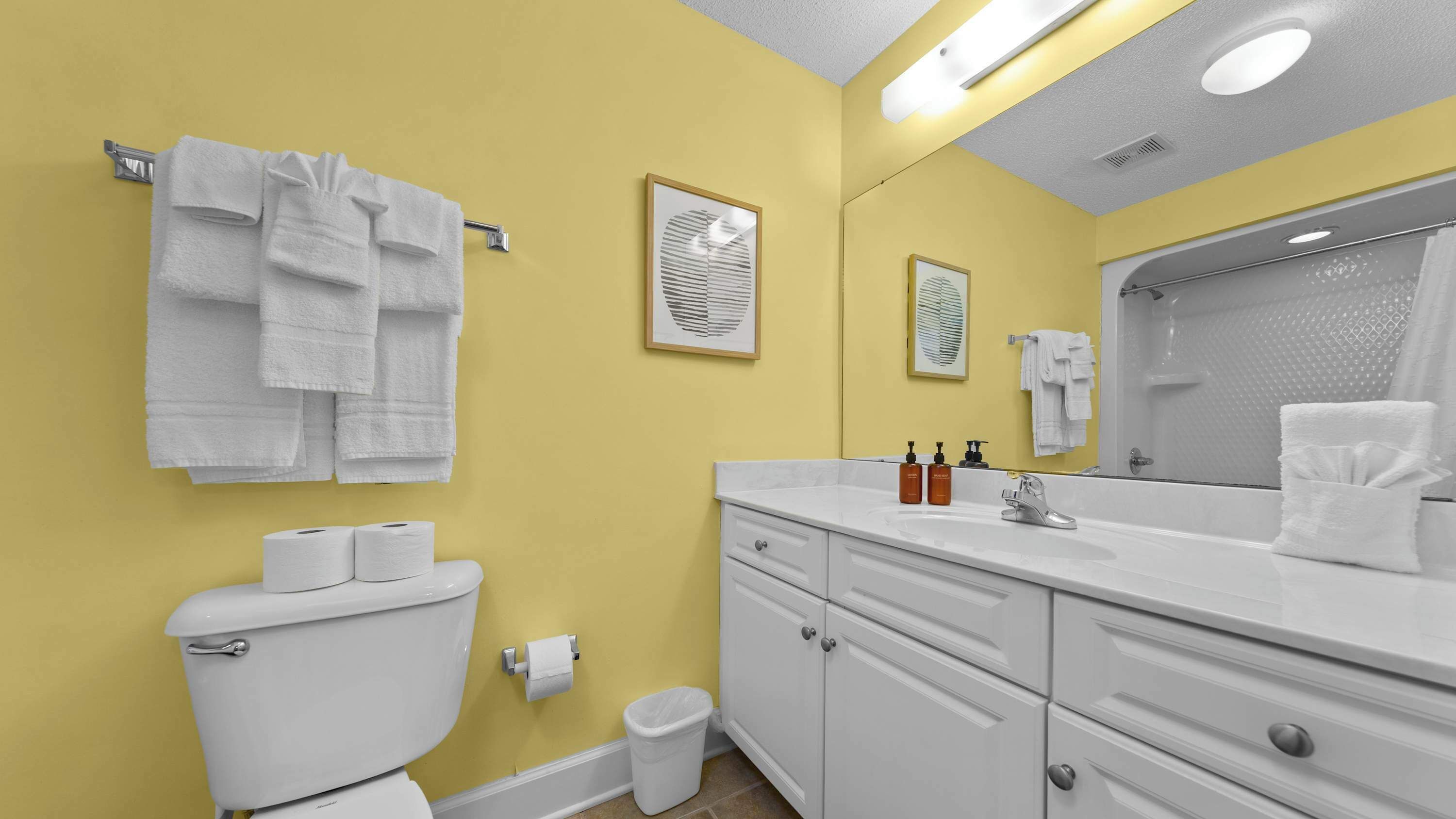 A bathroom with yellow walls, white fixtures, and multiple towels.