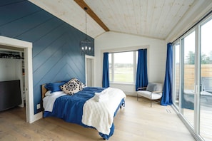 A bedroom with a bed, a chair, a desk, and a large window.
