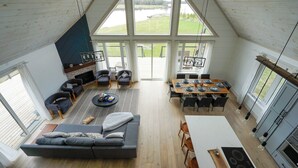 A spacious loft-style living area with a large dining table, a sofa, and a fireplace. - Muskoka 5BR Lakefront Cottage · Doe Lake · Sleeps 12+ · Pet-friendly · 4 Season (Gravenhurst)