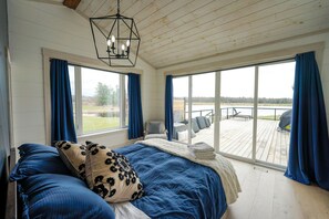 Un dormitorio con una cama grande, dos ventanas, vistas a una terraza y un aplique colgante.