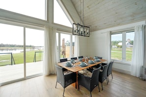 Un coin repas avec une table dressĂ©e pour six personnes, de grandes fenĂȘtres et une vue sur un lac.