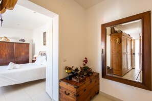 Une chambre avec une commode en bois, un lit recouvert de draps blancs et un grand miroir au mur.