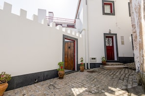 Une ruelle étroite pavée de pierres, bordée de bâtiments blancs, de portes rouges et de plantes en pot.