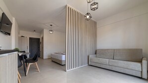 A modern living room with a sofa, a dining area with a table and chairs, and a kitchen area with a TV and a plant. - NS Apartments Nydri (Lefkada)